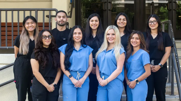 A group of post-baccalaureate dental program students pose together on outdoor steps.